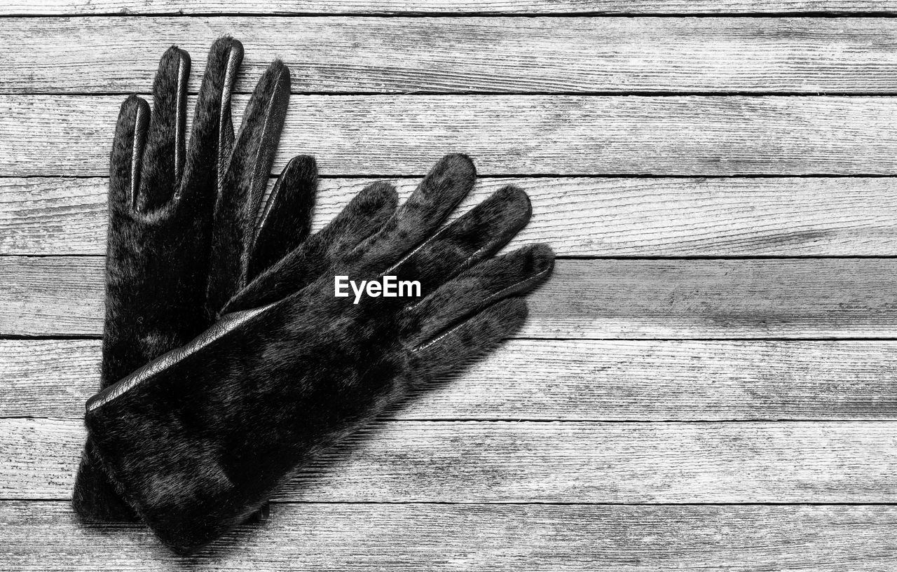 A pair of warm women's fur gloves on a wooden background, top view with copy space