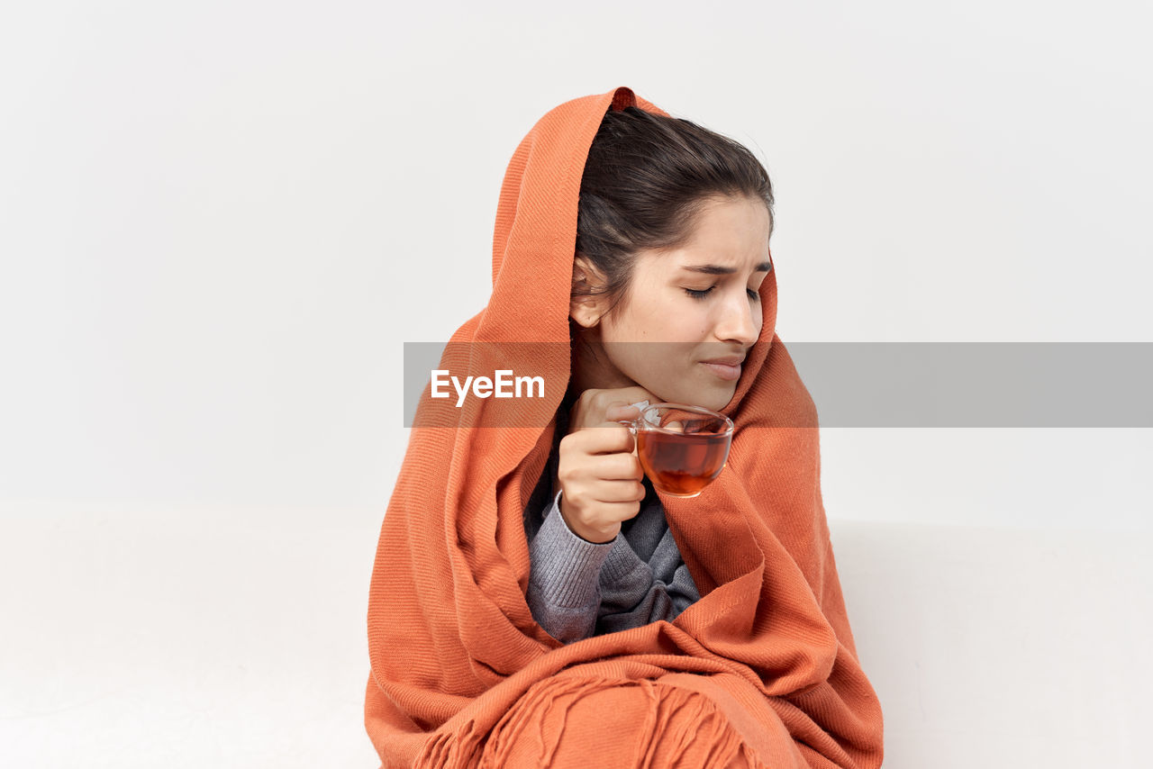 Young woman looking away while sitting against white background