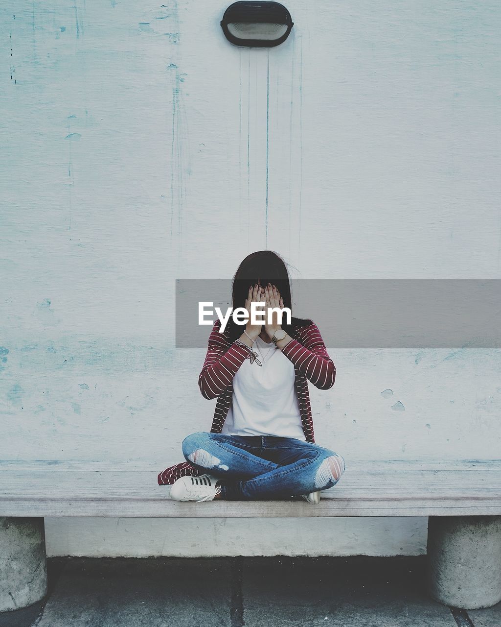 Woman covering face with hands while sitting against wall