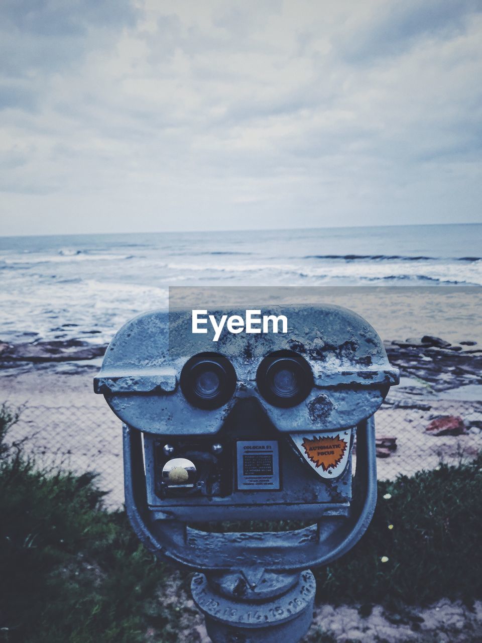 Close-up of coin-operated binoculars by sea against cloudy sky