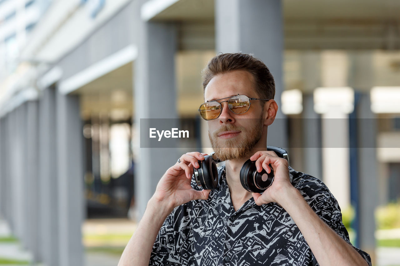 Portrait of a young man in sunglasses and headphones against the background of a modern city