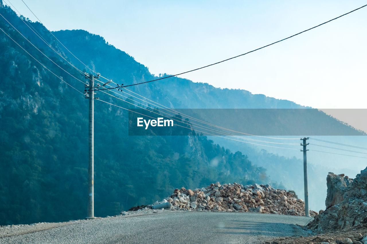 Electricity pylon by road against sky