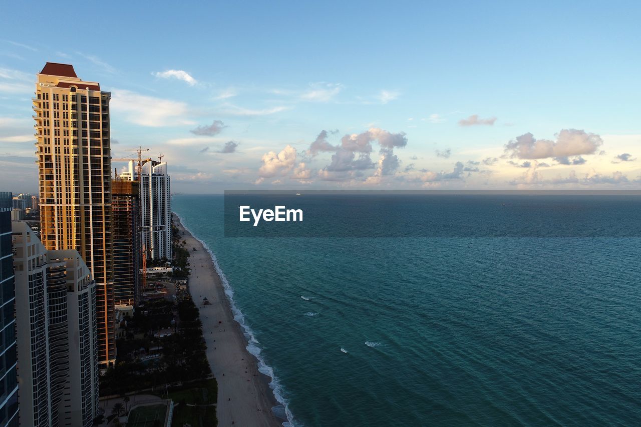 Sea by modern buildings against sky