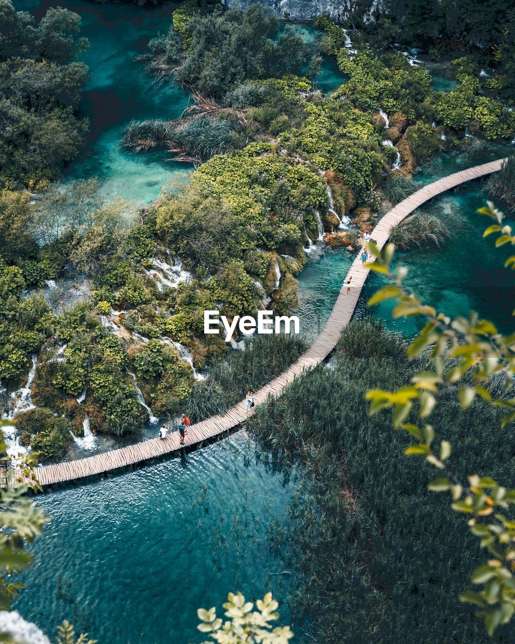 People walk across wooden path over lakes and waterfall at plitvice lakes national park.