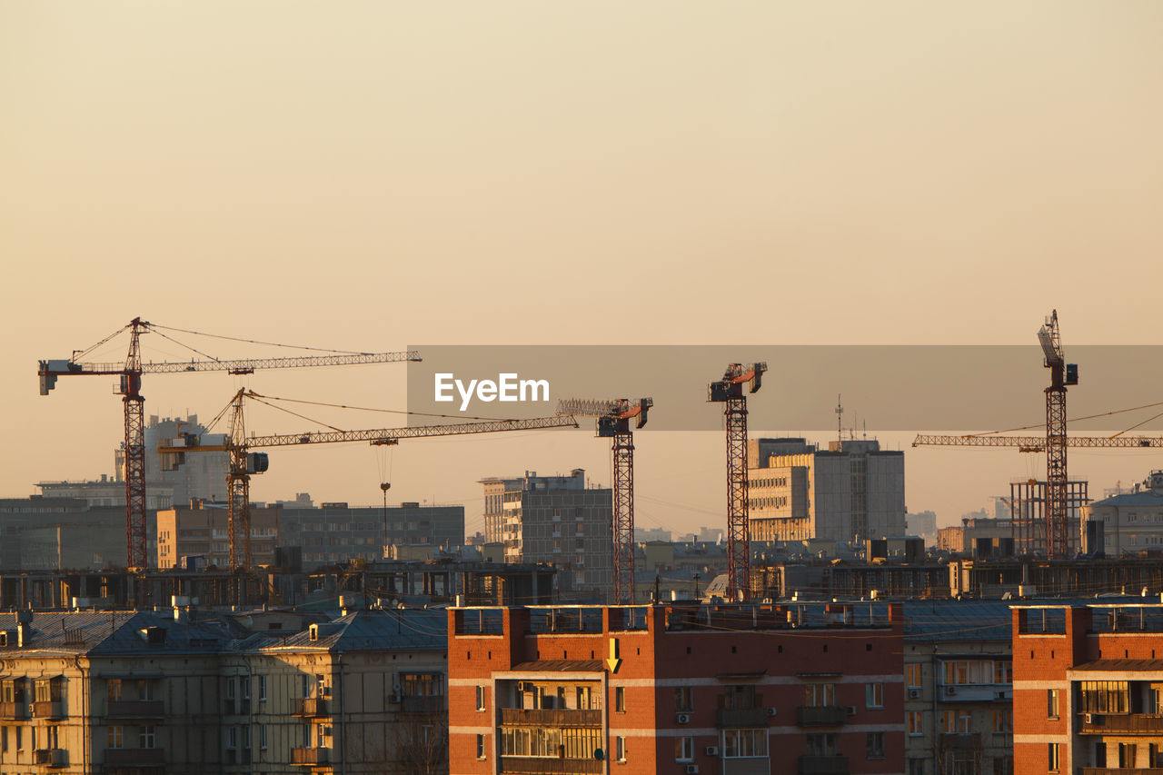 Buildings and cranes against sky during sunset