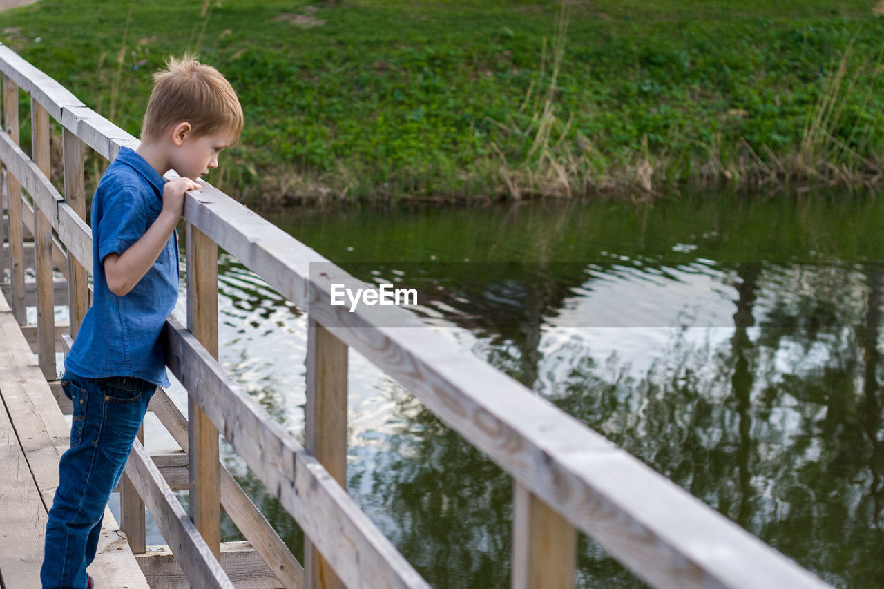 Side view of boy standing on bridge over lake