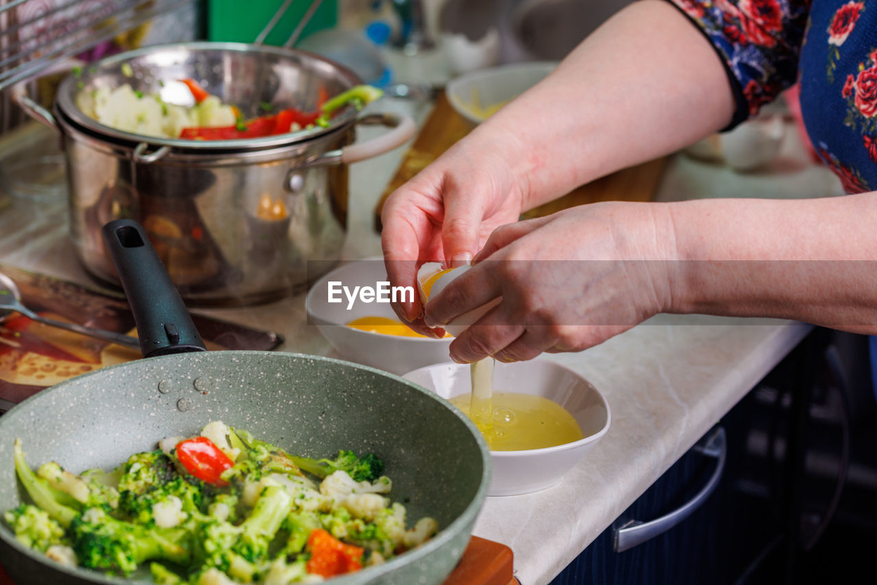 Senior caucasian woman hands breaking white chicken egg above the white bowl