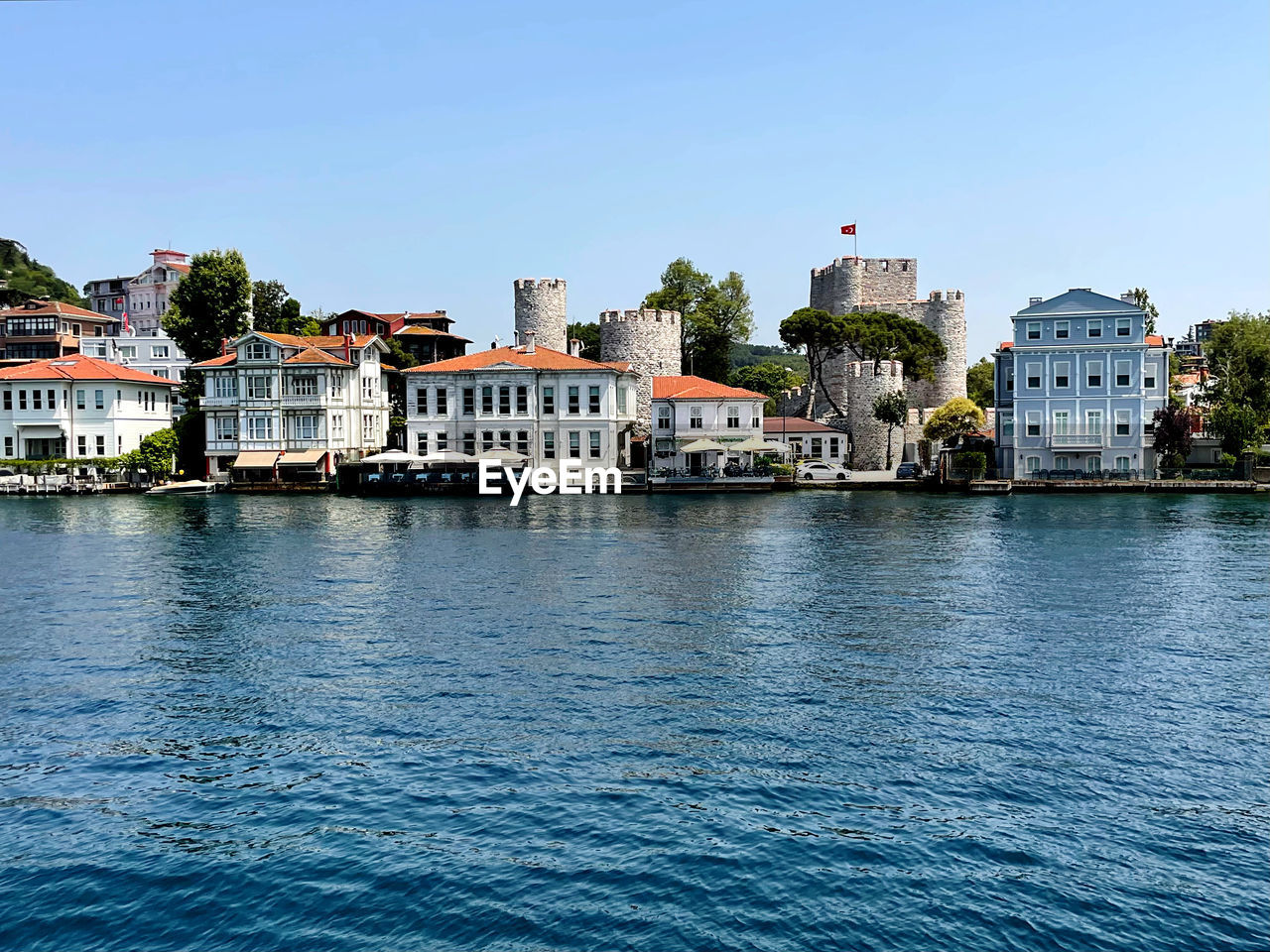 Buildings by river against clear blue sky