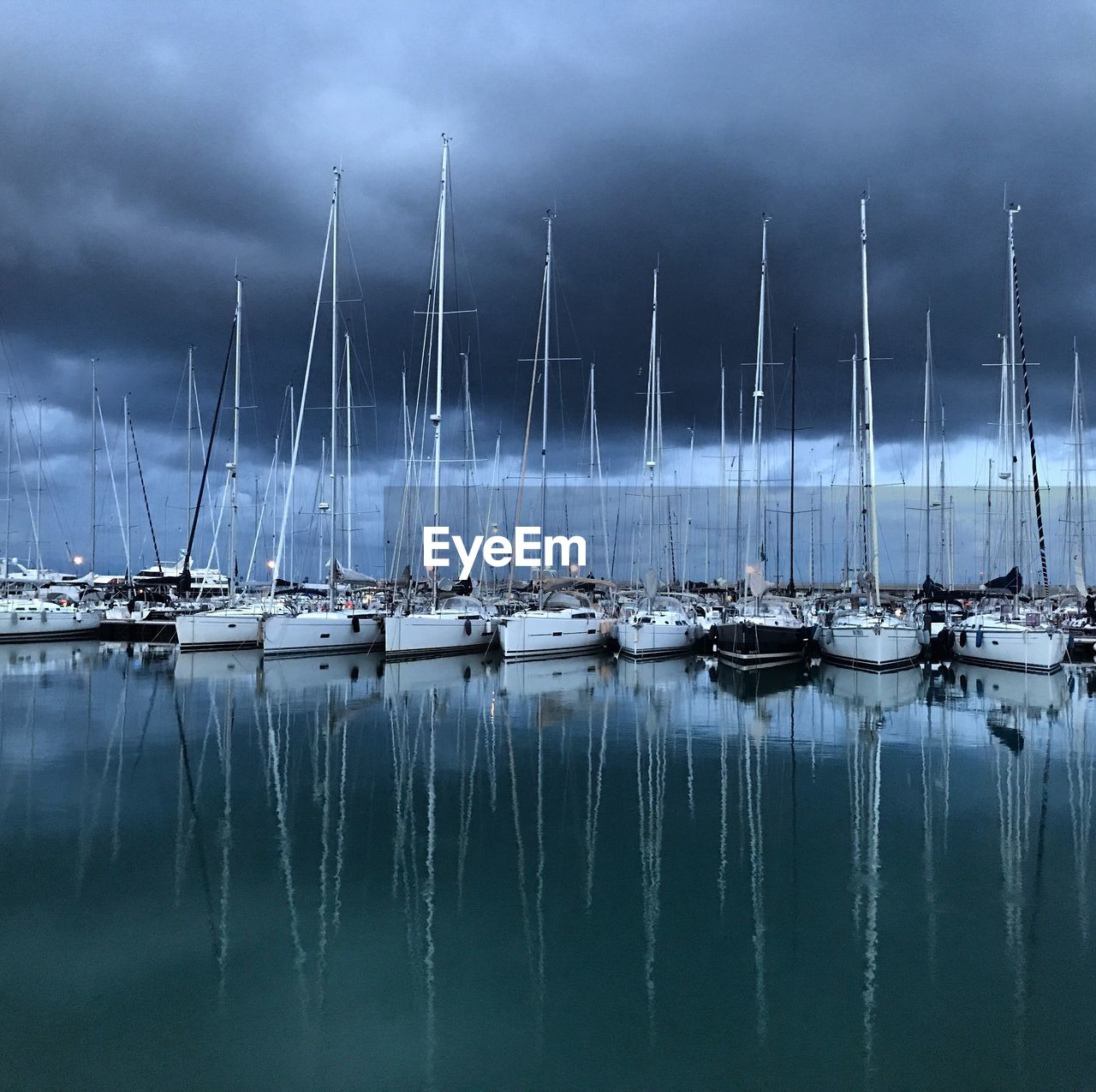 Sailboats moored in sea against cloudy sky