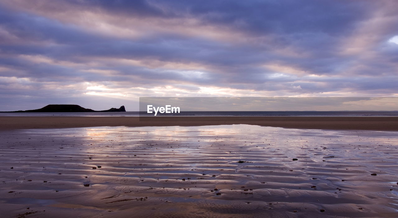 Scenic view of beach against cloudy sky at sunset