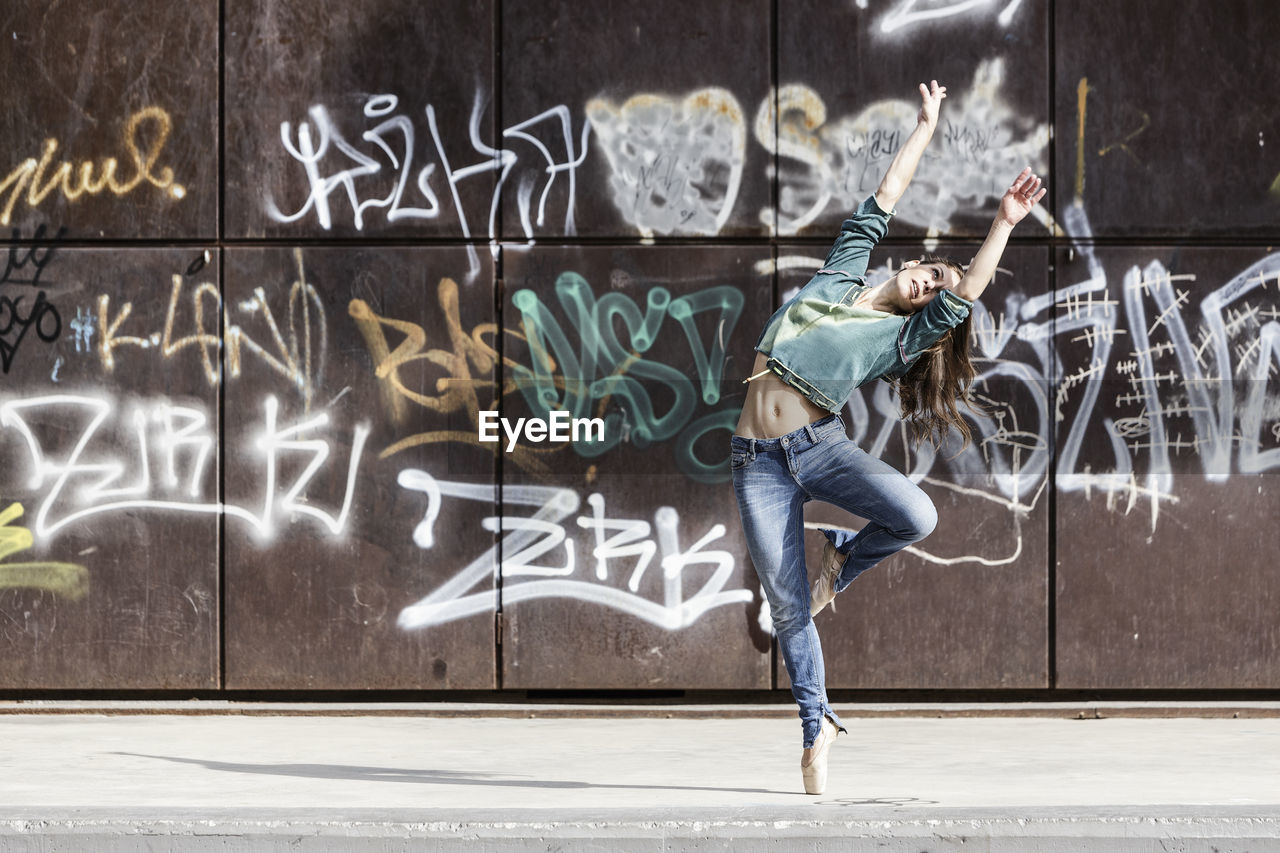 Full length of woman dancing against graffiti on wall