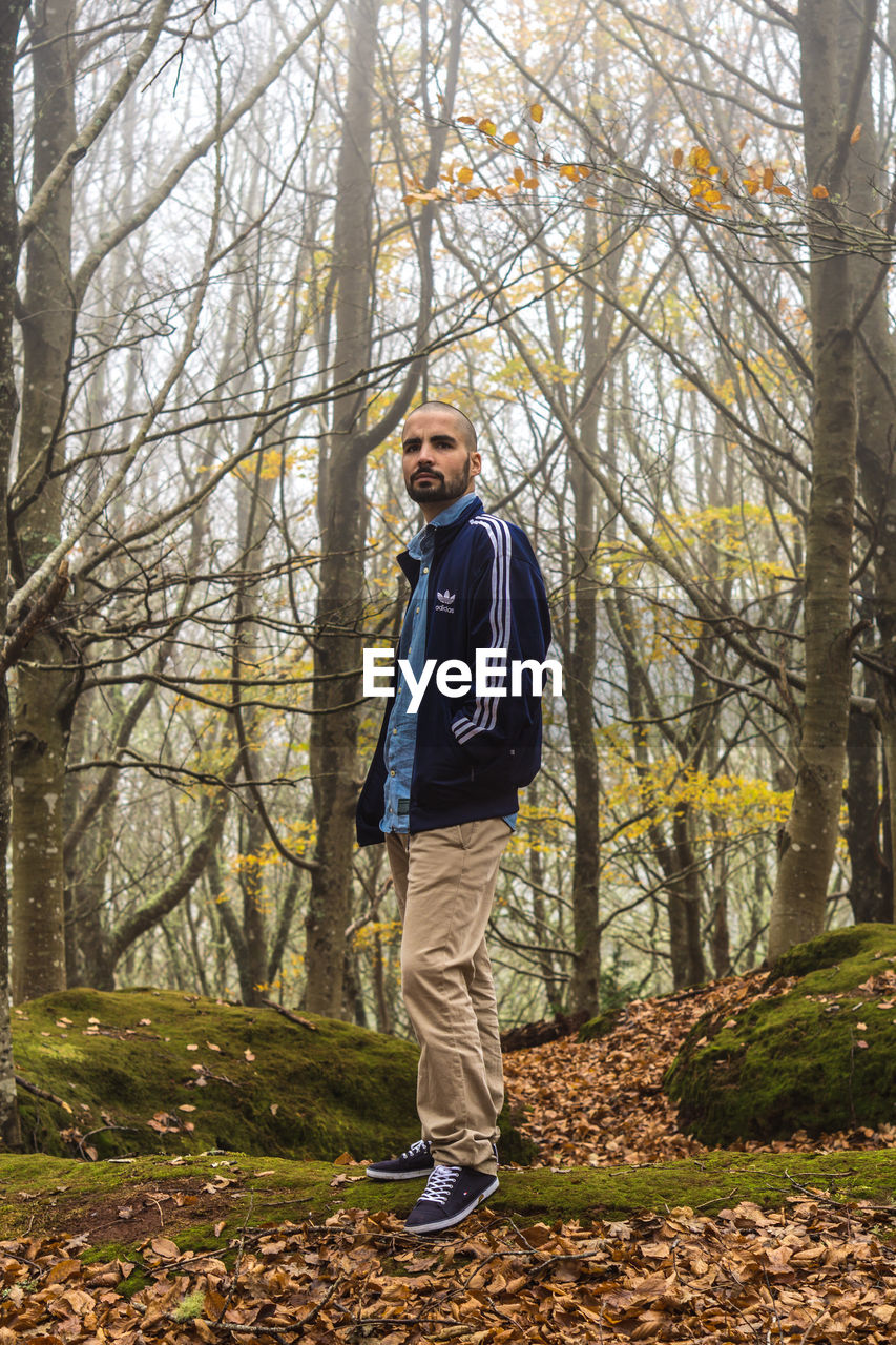 PORTRAIT OF MAN STANDING BY TREE IN FOREST