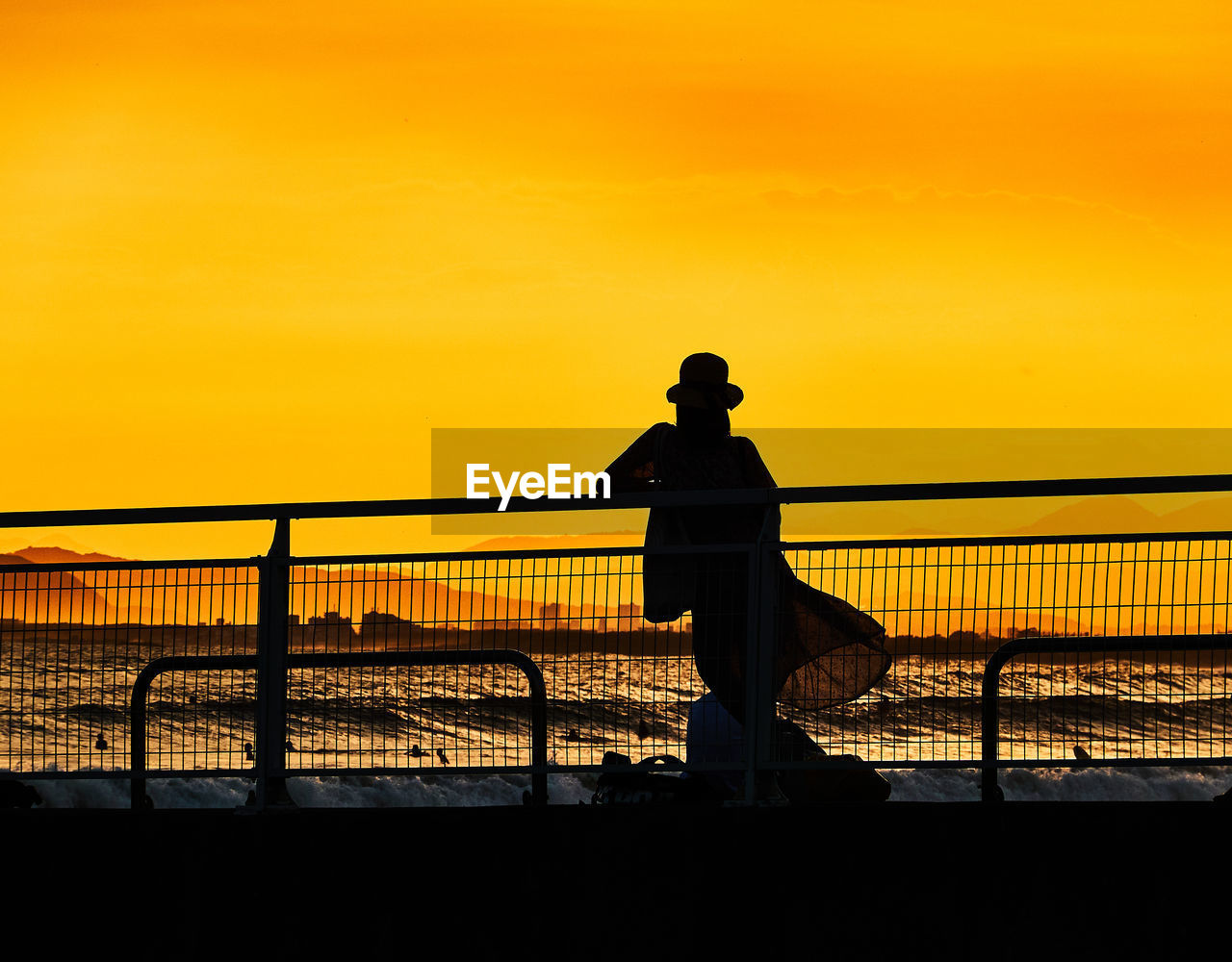 Silhouette women standing on bridge against sky during sunset