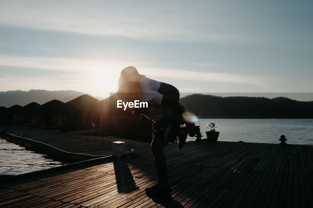 Man on pier over lake against sky during sunset