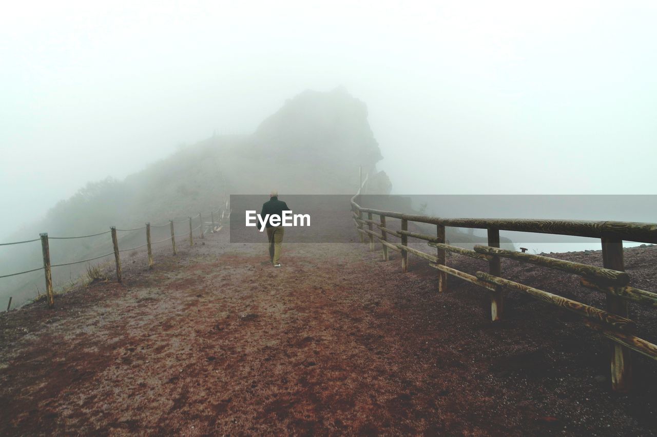 Rear view of man walking on mountain during foggy weather