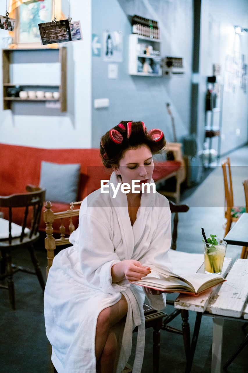 Woman wearing hair curlers while sitting on table at beauty spa