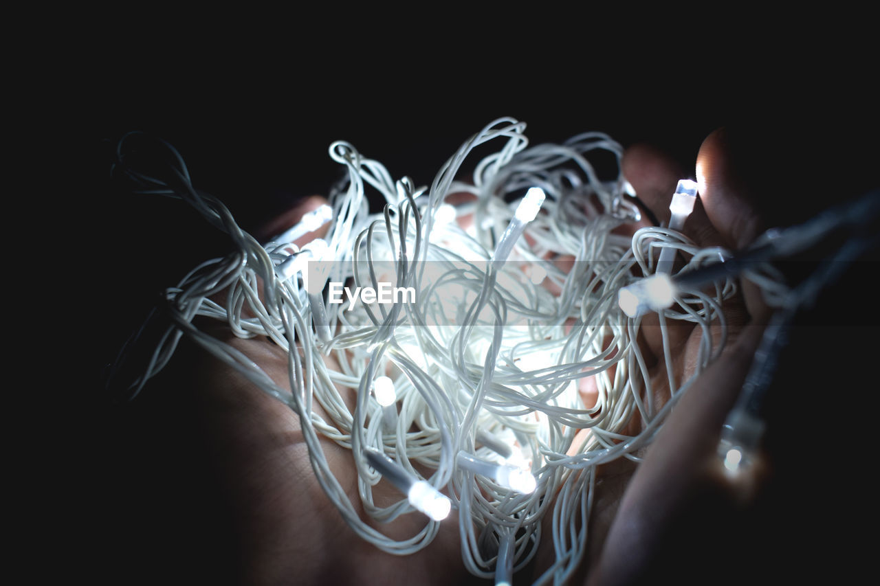 Close-up of human hands holding illuminated sting lights against black background