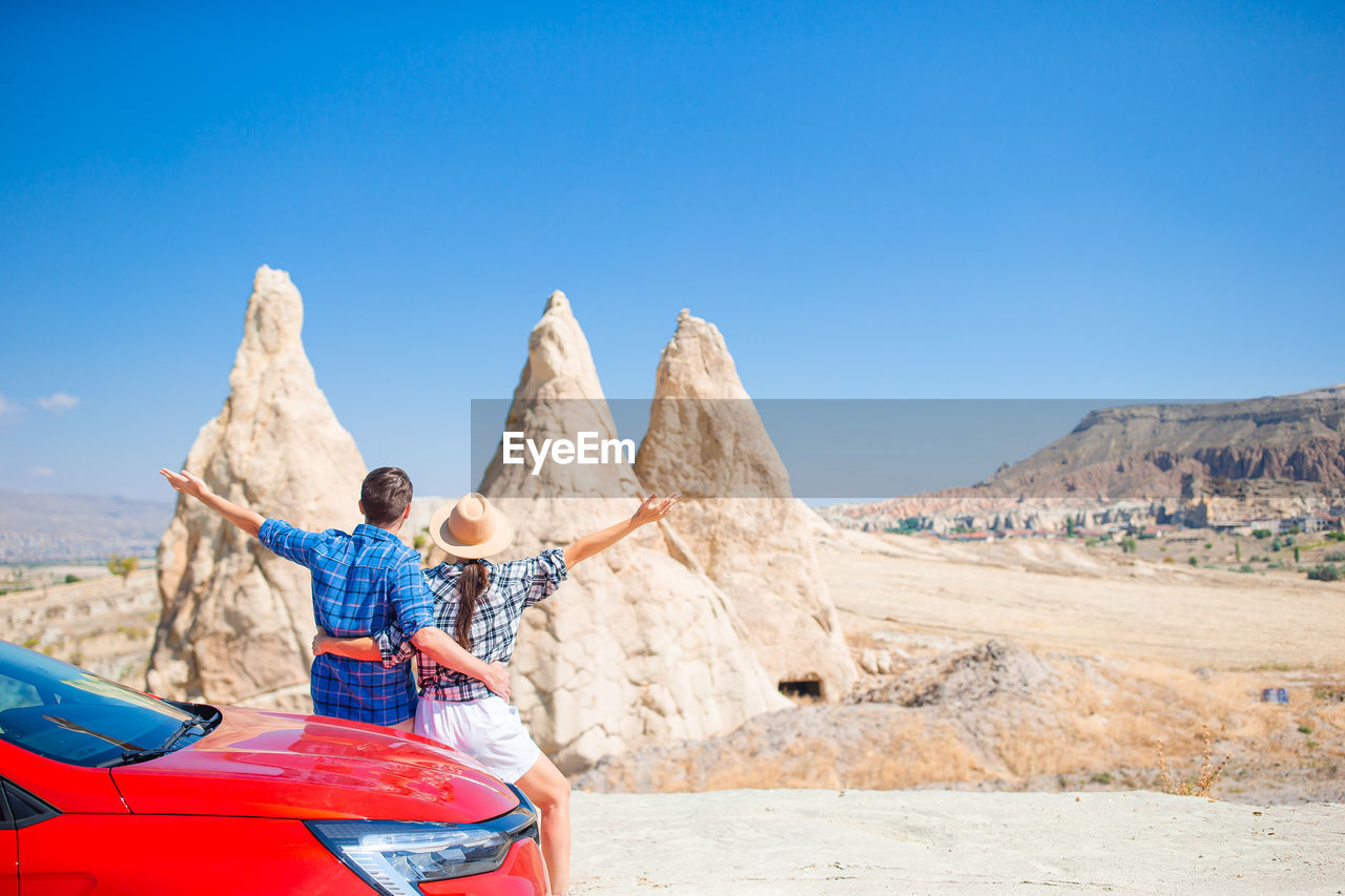 rear view of woman sitting on rock formations against clear blue sky