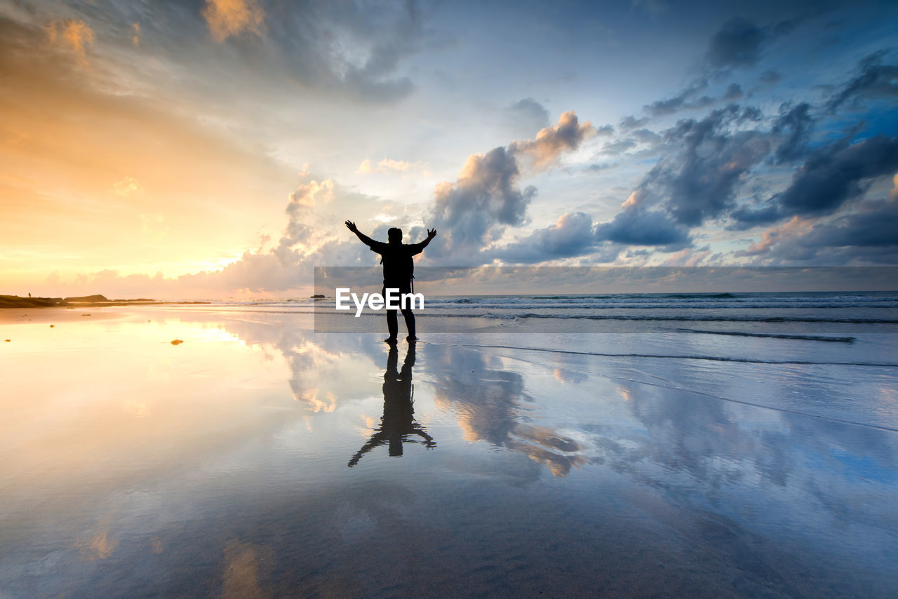 Silhouette man standing on shore at beach against sky during sunset