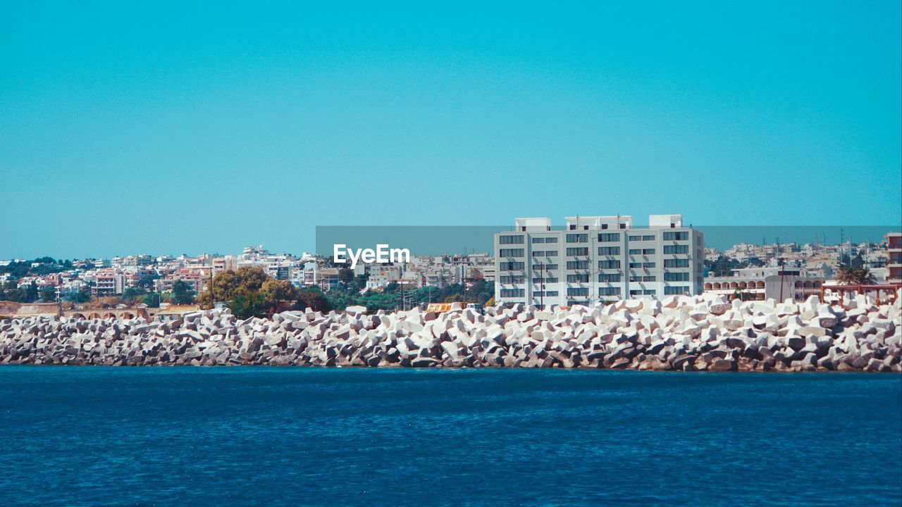 Sea by buildings against clear blue sky