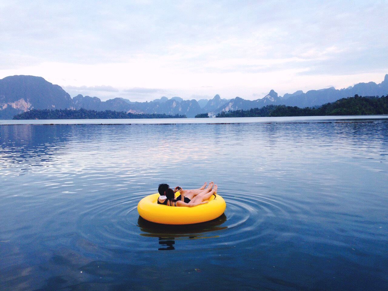 Couple on inflatable ring at lake against sky