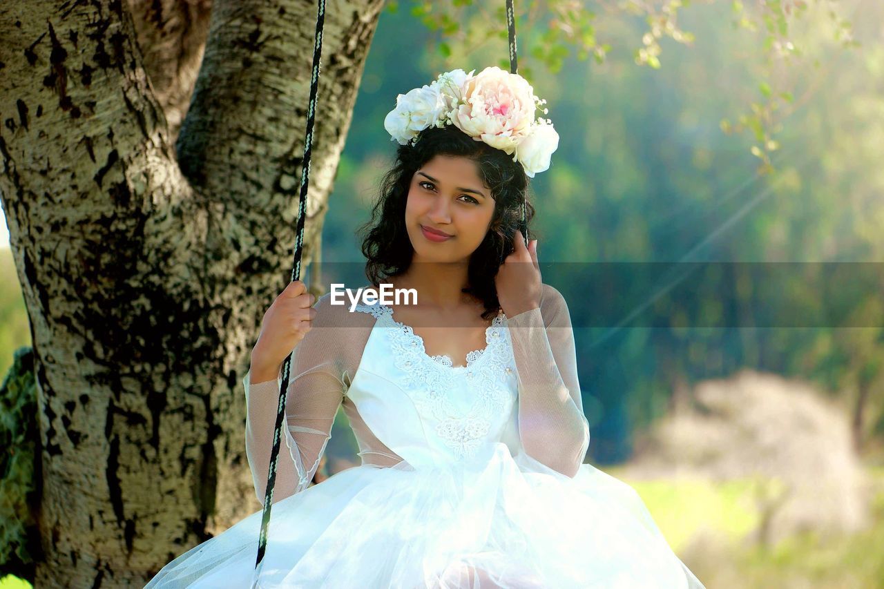 Portrait of smiling bride wearing wedding dress standing at park