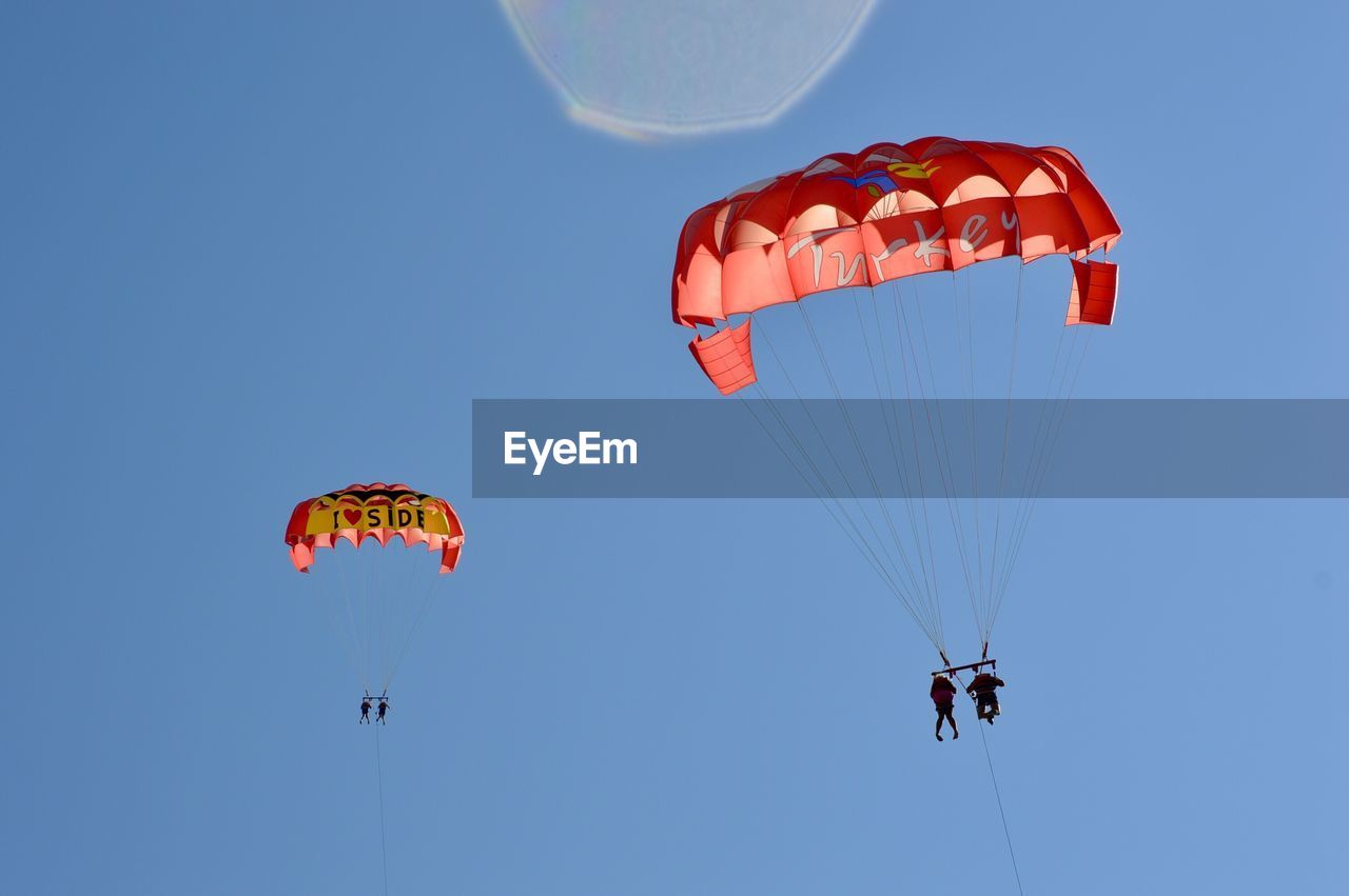 Low angle view of people parasailing against clear blue sky