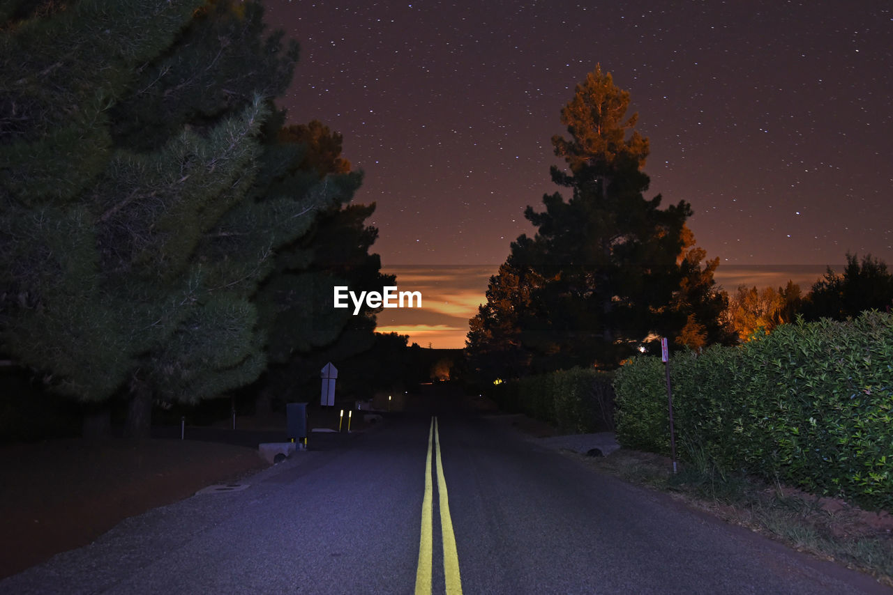 Road amidst trees against sky at night