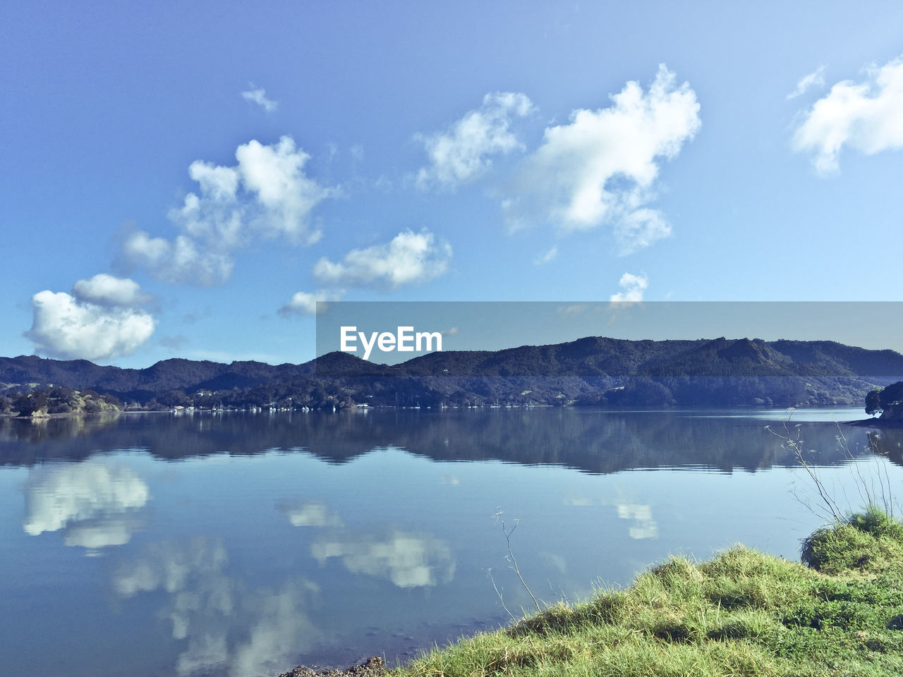 REFLECTION OF CLOUDS IN CALM LAKE AGAINST MOUNTAIN RANGE