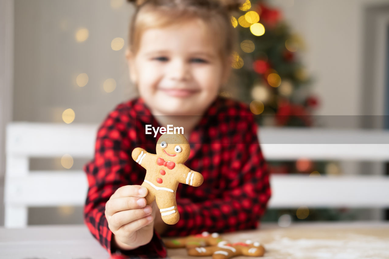 Little girl in red pyjama holding decorated christmas gingerbread men cookie. selective focus