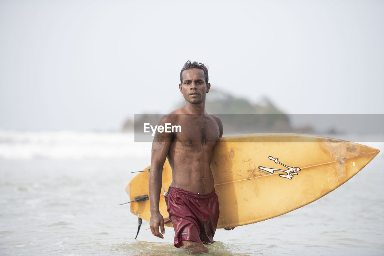 YOUNG MAN STANDING ON BEACH AGAINST SEA