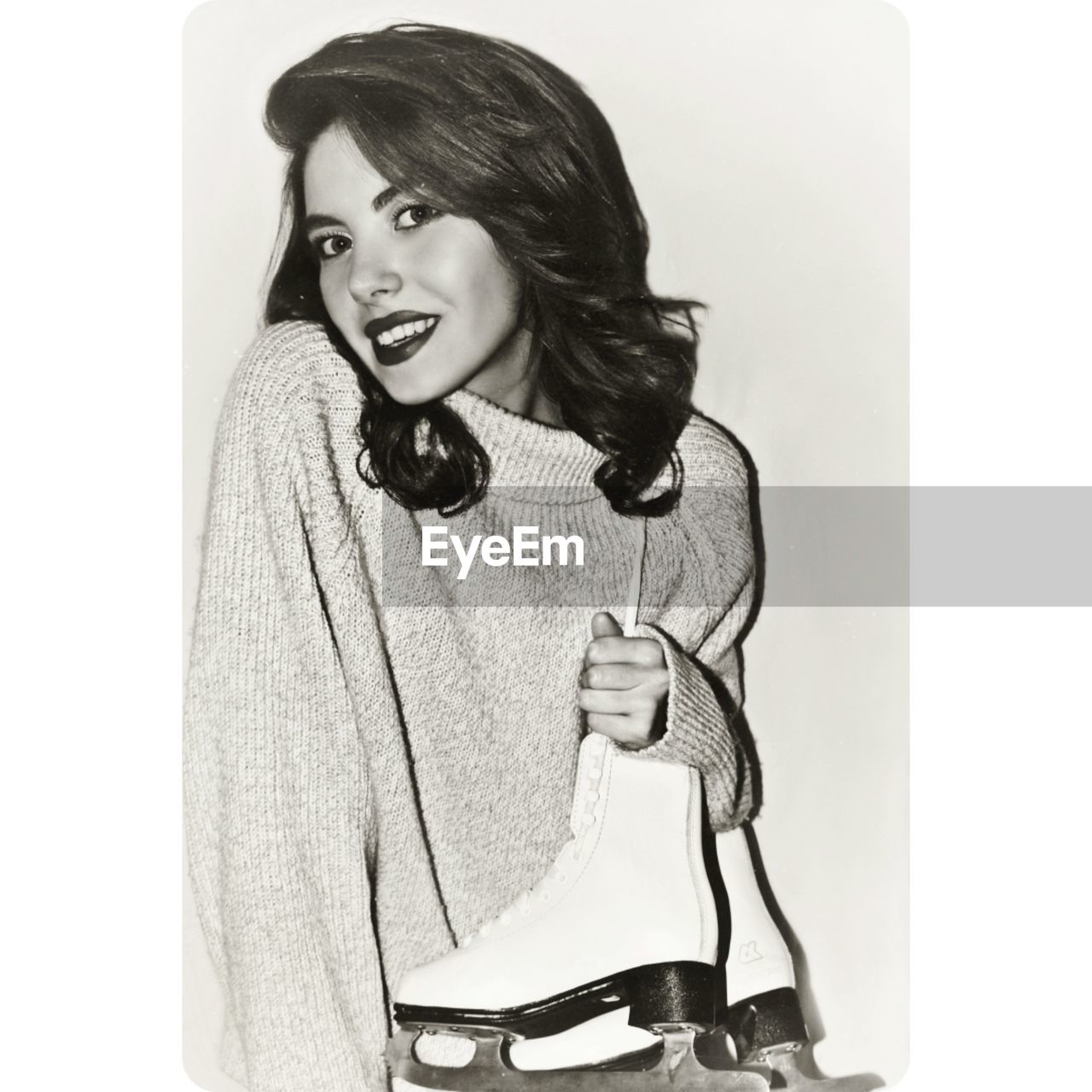 Portrait of happy young woman holding ice skates against gray background