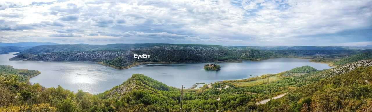 Panoramic view of river by mountains against cloudy sky