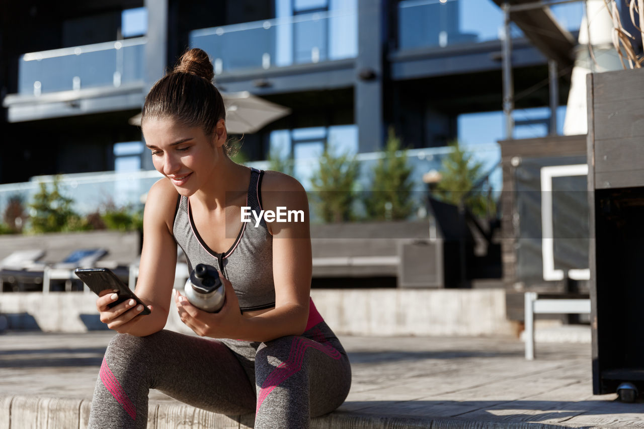 Young woman using smart phone while sitting outdoors