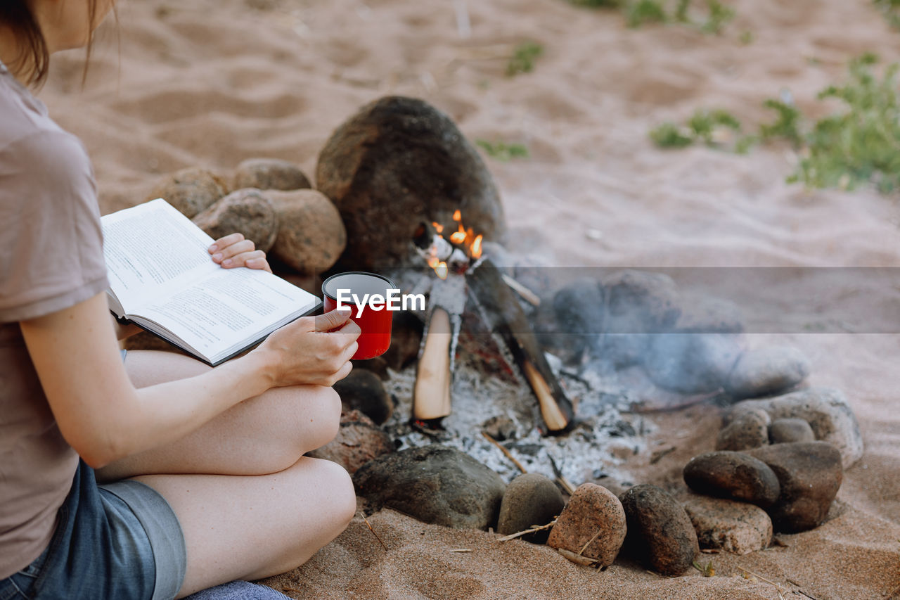 Woman's hand holds a red cup over a campfire in nature. campfire on a hike in the forest. traveling