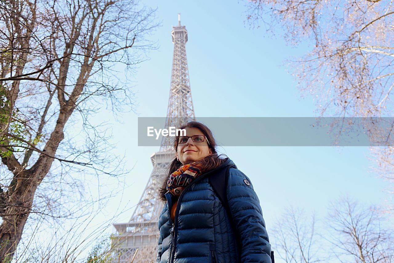 Low angle view of woman looking away while standing against eiffel tower and sky