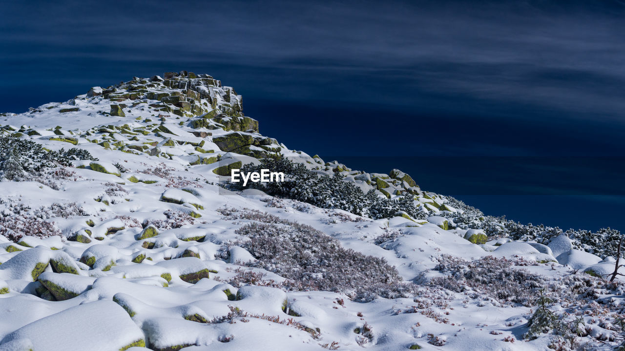 Snow covered rocks in sea against sky