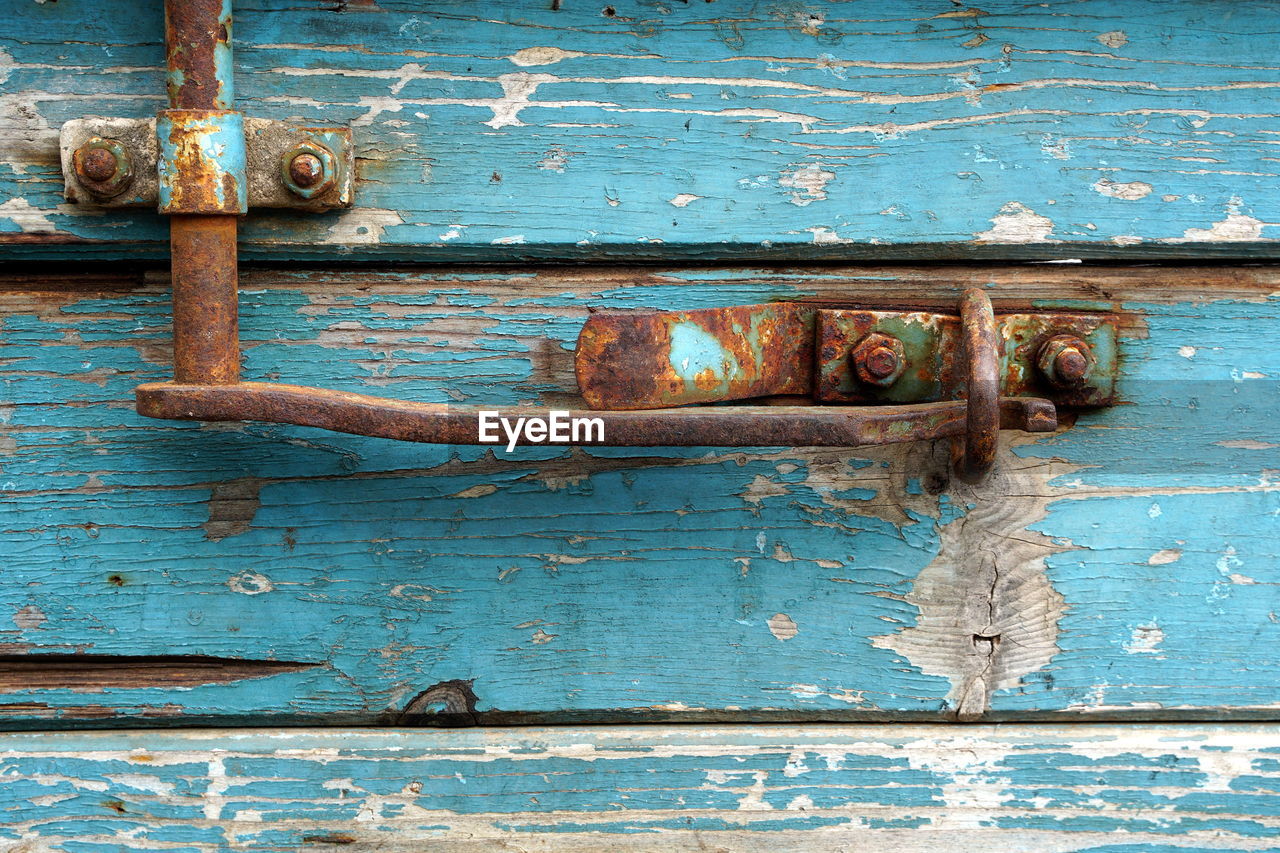 FULL FRAME SHOT OF RUSTY METAL DOOR WITH OLD WEATHERED WOODEN WALL