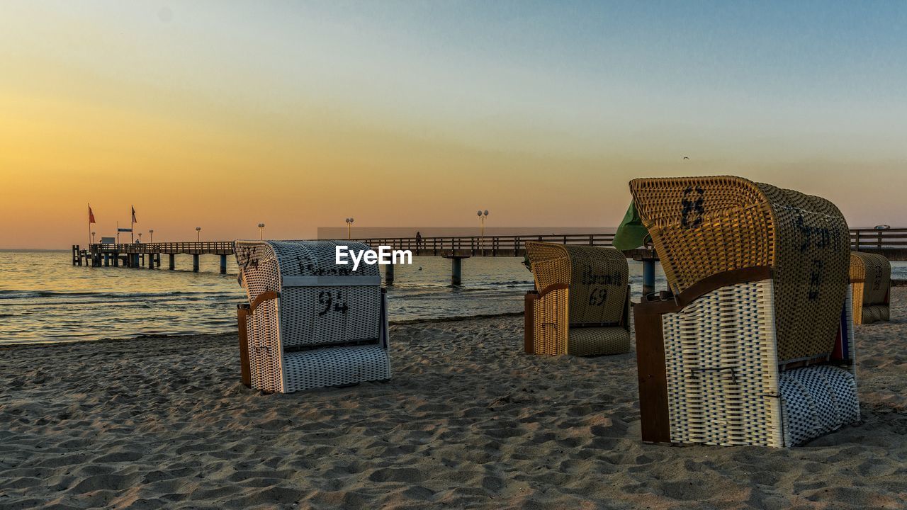 Hooded beach chairs at shore during sunset