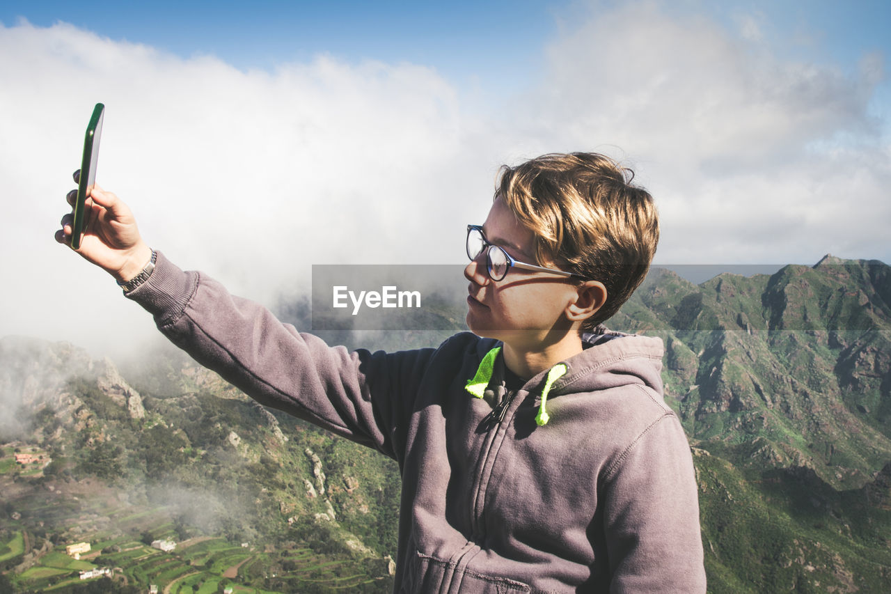 Boy doing selfie while standing against mountain range