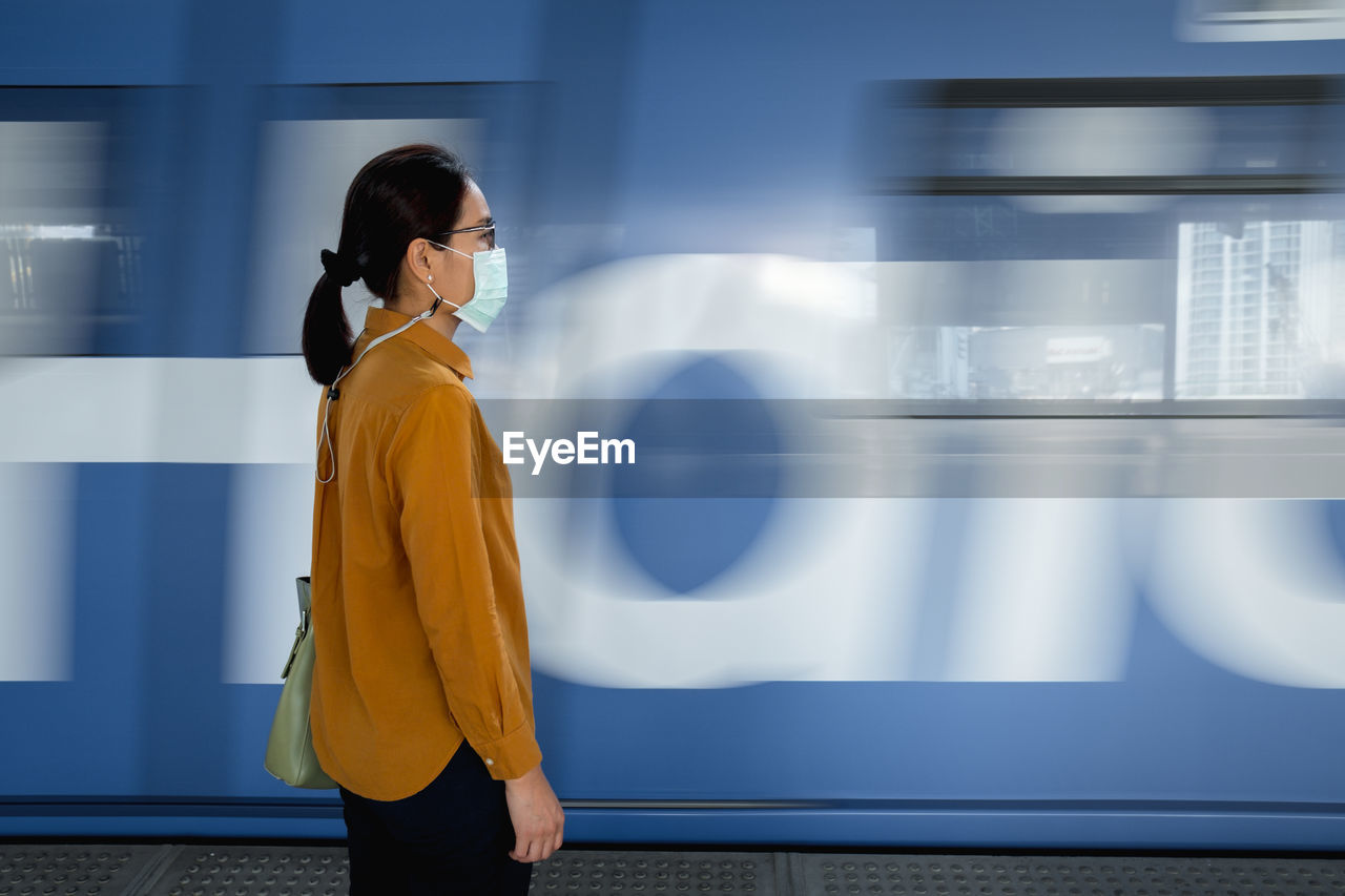 Side view of woman wearing mask standing against train