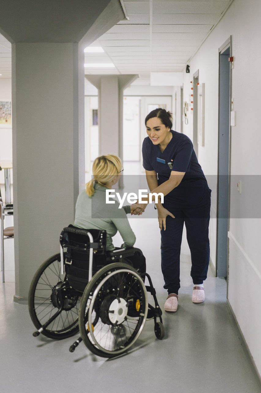 Smiling female nurse greeting patient sitting on wheelchair at hospital