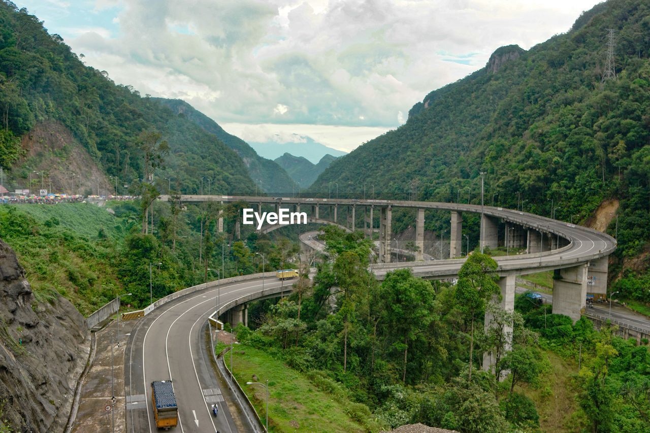 Bridge over road by mountains against sky