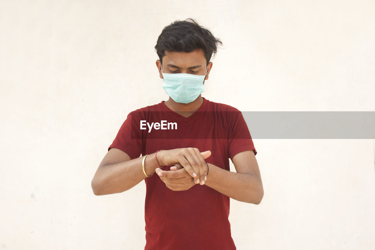 Young man wearing flu mask using hand sanitizer standing against white background