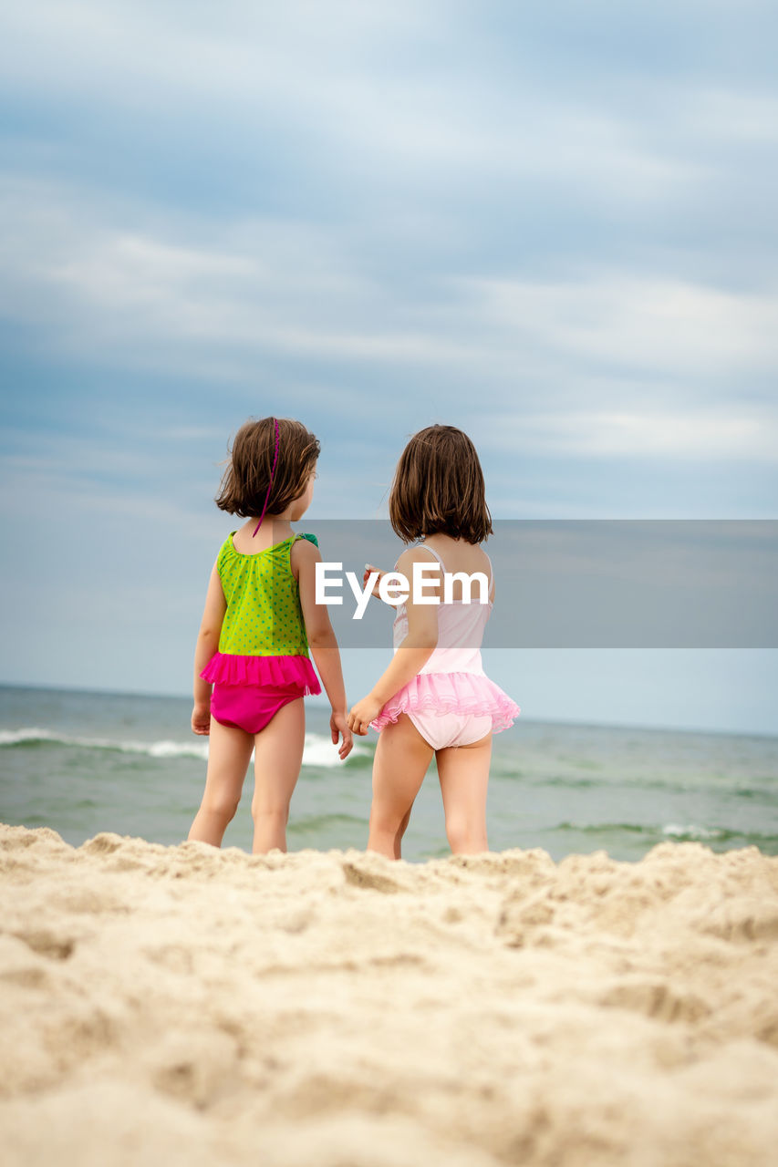 REAR VIEW OF WOMEN ON BEACH AGAINST SEA