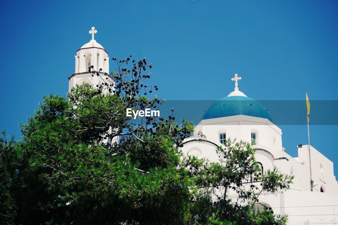 Low angle view of trees and building against blue sky