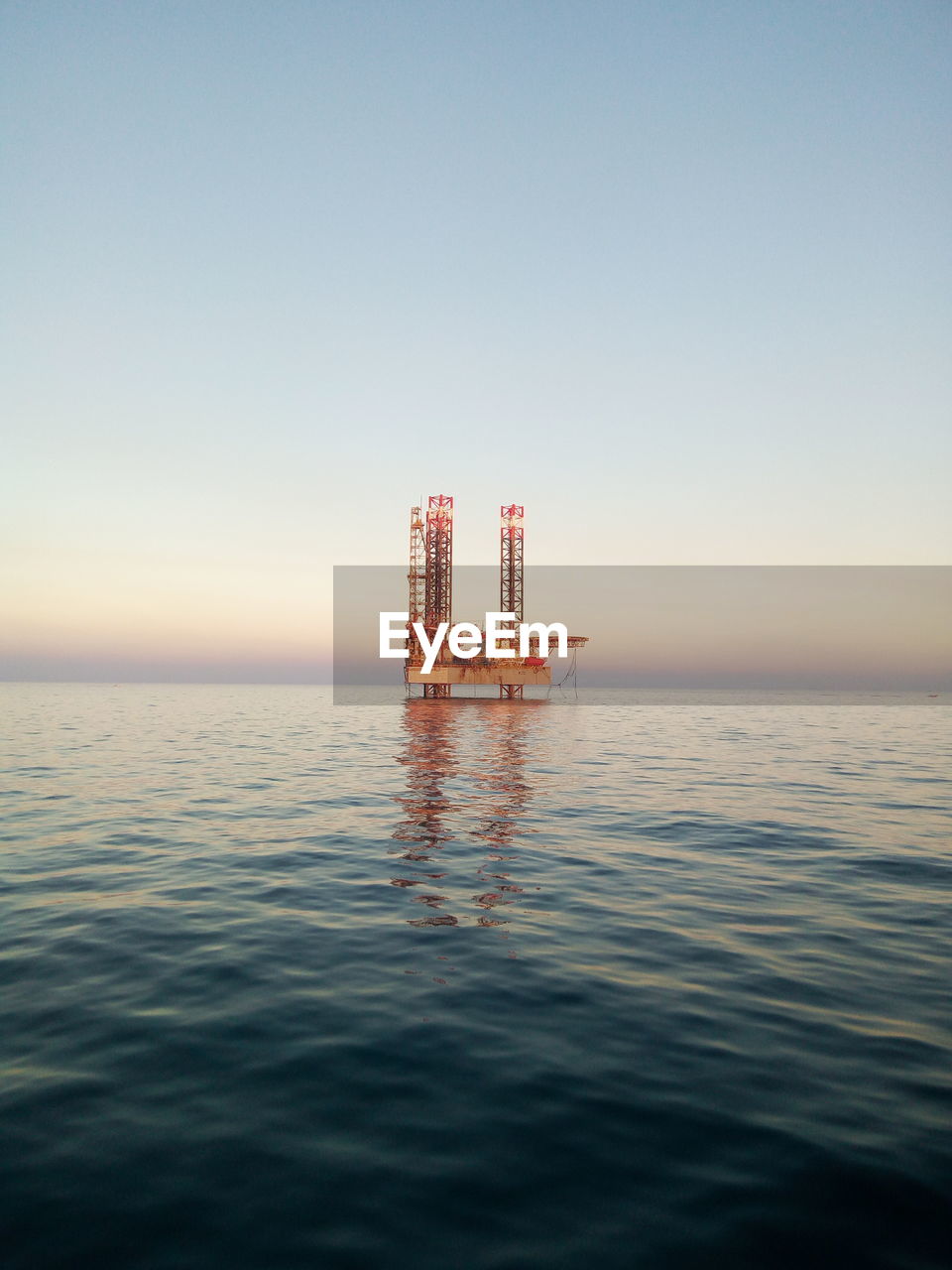 Offshore platform in sea against clear sky during sunset