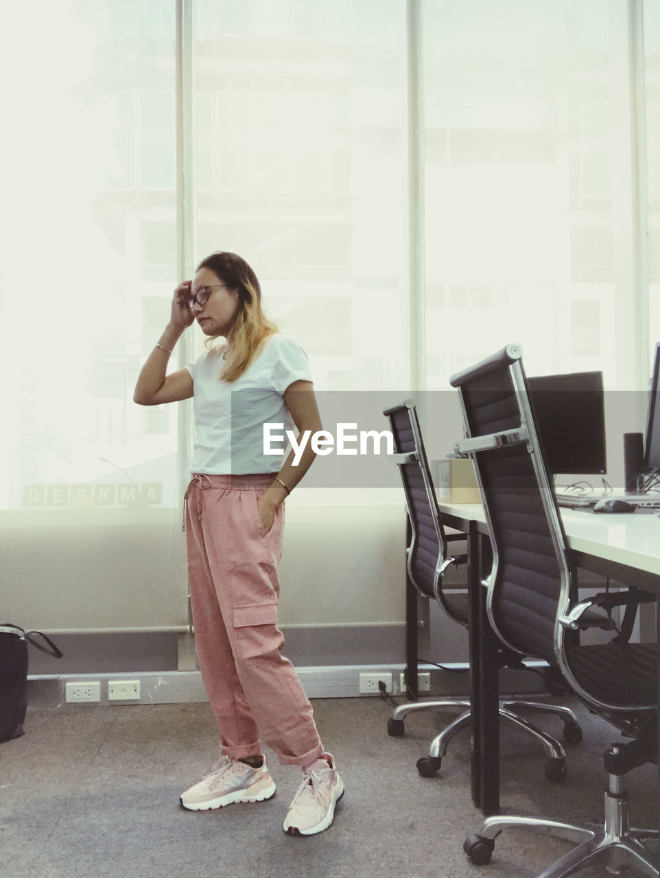 FULL LENGTH PORTRAIT OF WOMAN STANDING BY WINDOW IN OFFICE