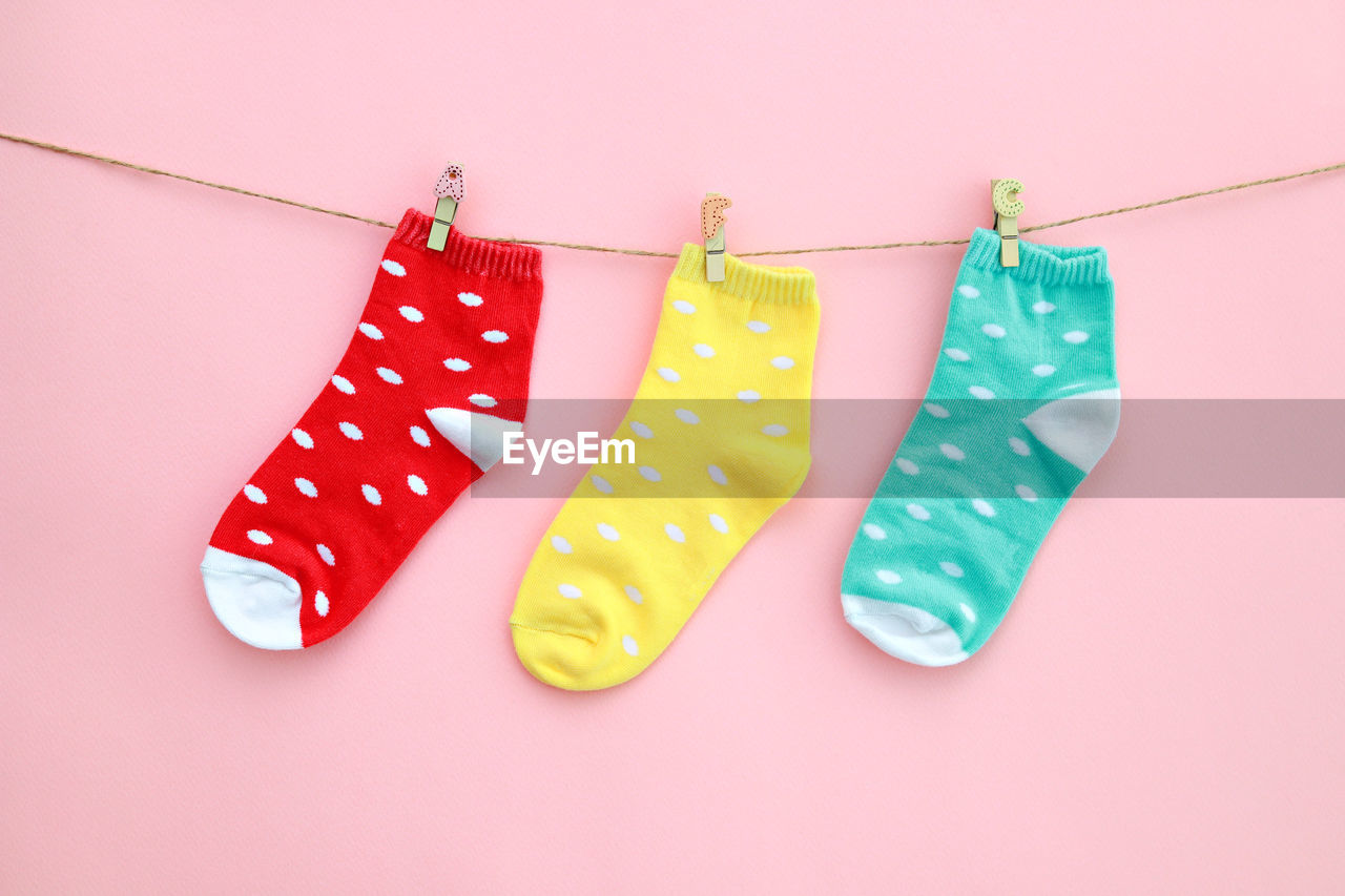 Multi colored socks hanging on clothesline over pink background