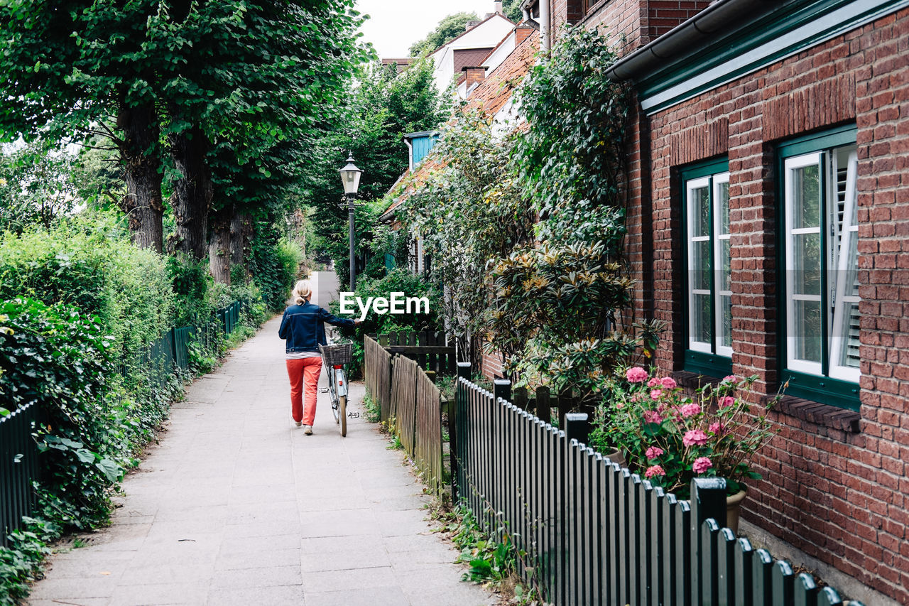 Rear view of woman walking with bicycle by house